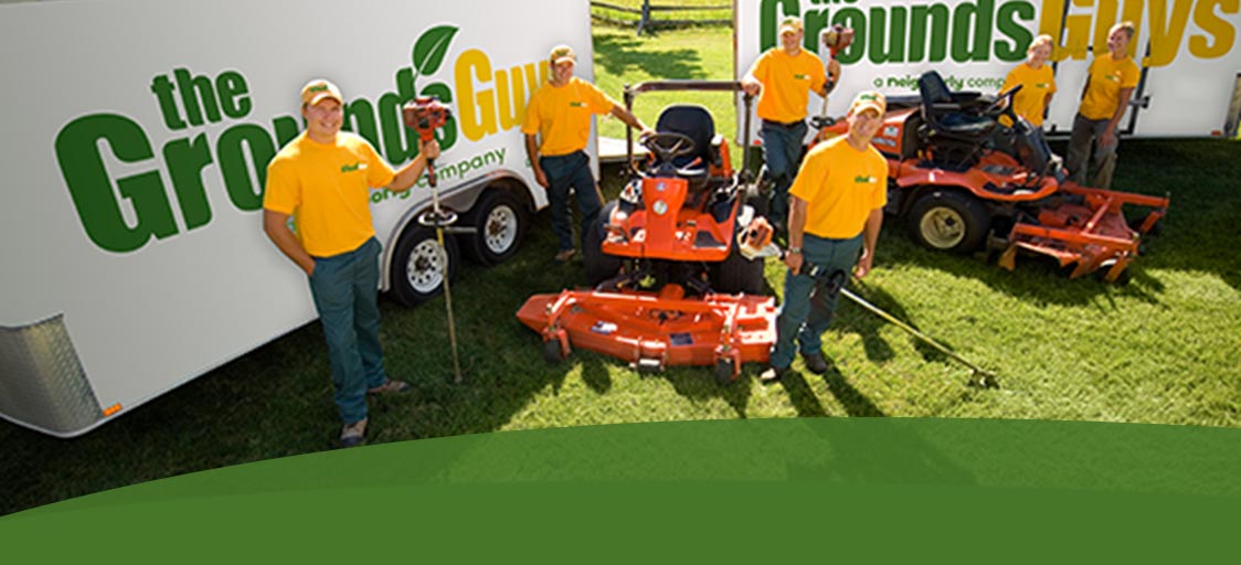 The Grounds Guys workers with branded trucks and landscaping equipment